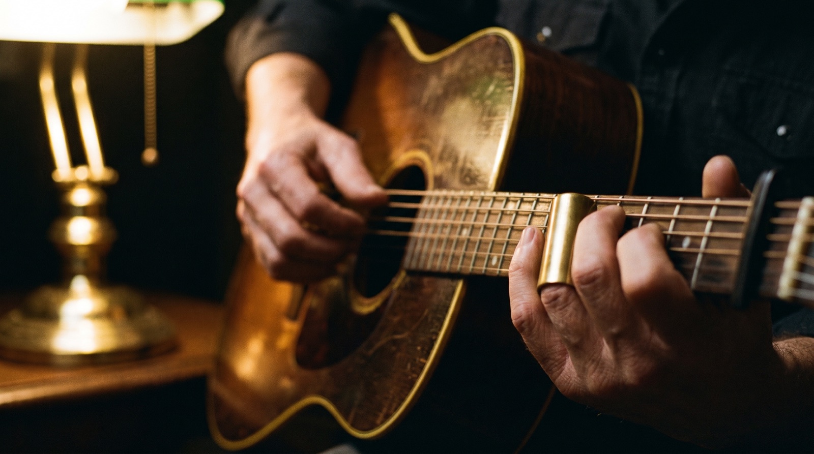 Gros plan de mains qui jouent d’une guitare acoustique près d’une lampe de laiton